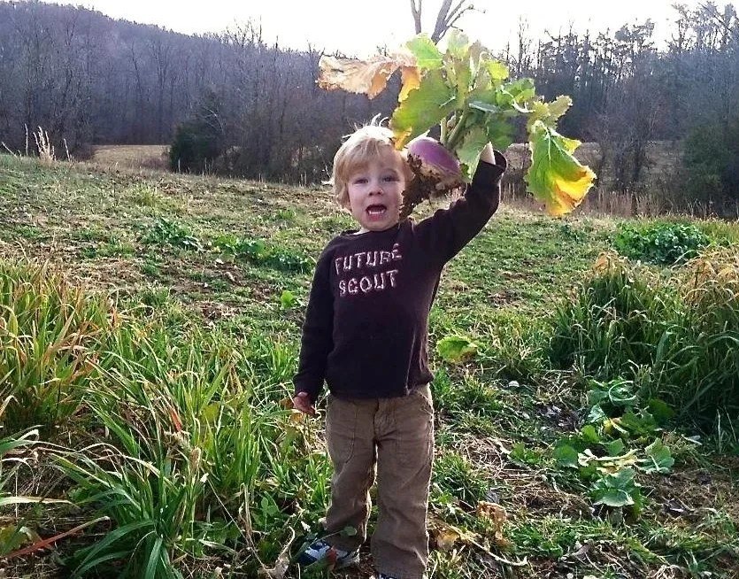 A little boy holding up vegetables